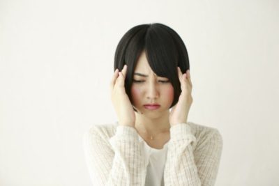 頭痛で頭を押さえて辛そうにしている女性の写真。肩こりからくる頭痛のイメージ。