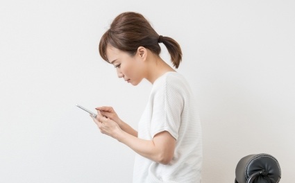 スマートフォンを長時間見て首が前に出ている女性。ストレートネックによる肩こりの例。