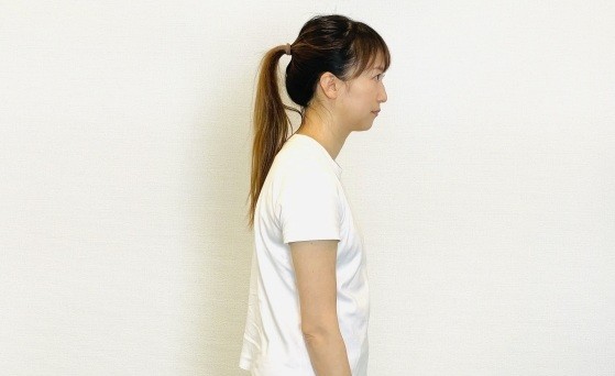 猫背で肩が前に巻き込んだ女性の横向き姿勢。姿勢の乱れが肩こりの原因になる例。