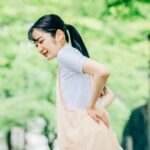 残暑疲れで腰痛が悪化しやすい産後ママが、公園で腰を痛めて腰を押さえている様子