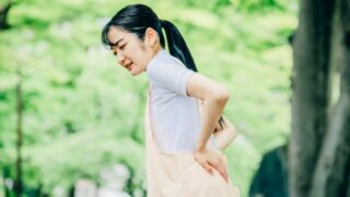 残暑疲れで腰痛が悪化しやすい産後ママが、公園で腰を痛めて腰を押さえている様子