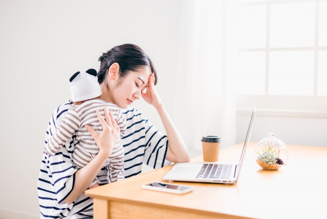 育児をしながら仕事をする女性の写真。ストレスや生活習慣の乱れによる腰痛を表現