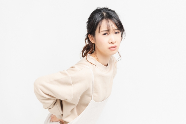 腰に手を当てて痛みを感じている女性の写真。腰痛に悩む様子を表現