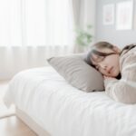 産後の女性がベッドで寝返りを打つ様子。骨盤のゆがみによる腰の違和感を感じているイメージ写真。
