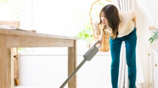 年末に中腰で掃除機をかける女性。