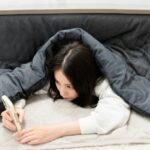 こたつで不良姿勢でスマホを見る女性