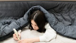 こたつで不良姿勢でスマホを見る女性