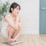 連休中に食べ過ぎて、体重計の上で悩む女性