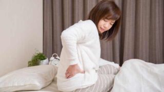寝返りした時の腰痛で、起き上がって腰を手で押さえる女性